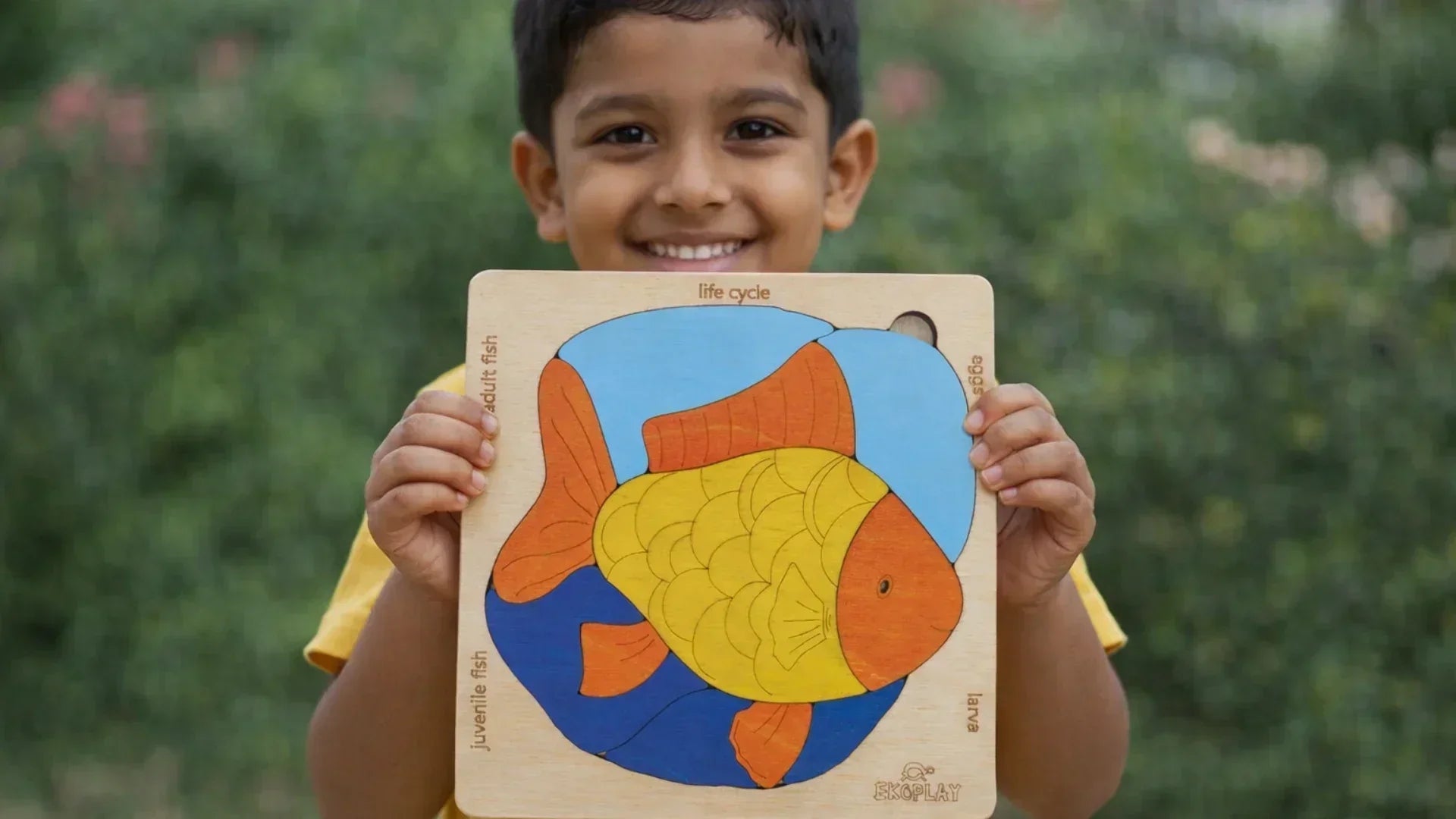 Smiling child holding a colorful wooden fish life cycle puzzle toy, promoting early learning, problem-solving skills, hand-eye coordination, and cognitive development through educational play.